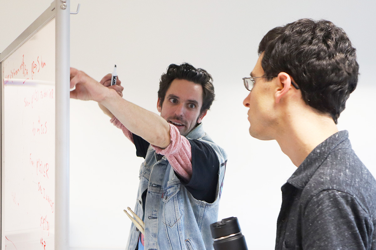 Student works excitedly at whiteboard while faculty member looks on