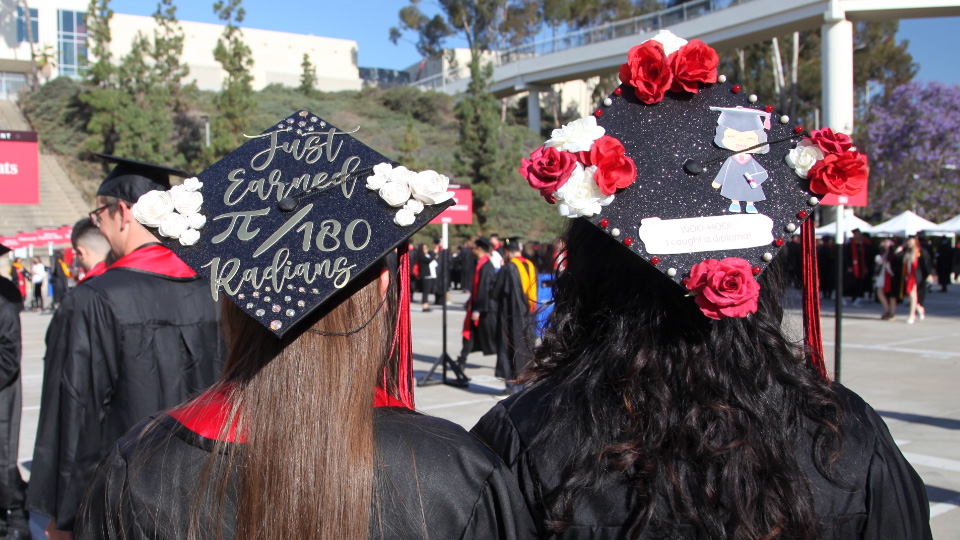 Two people with long hair wearing graduation caps. The one on the left says "Just earned pi/180 radians"