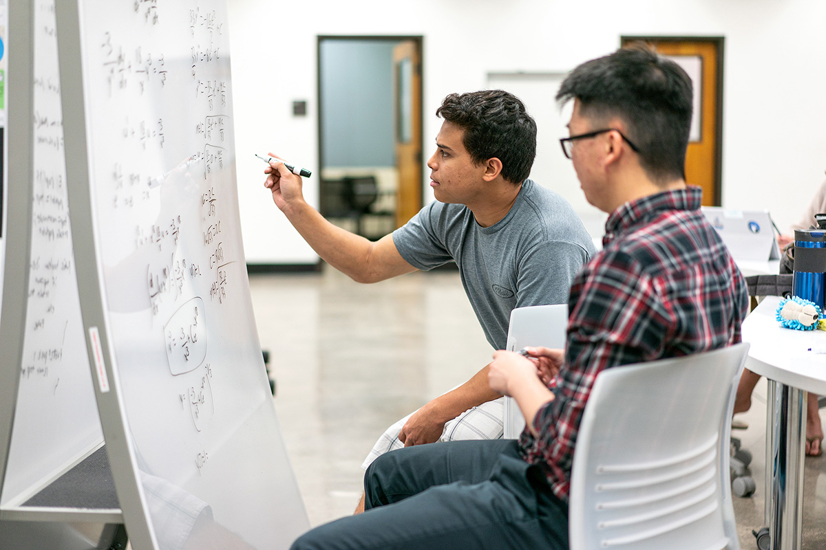 Two students work on math problems on a whiteboard