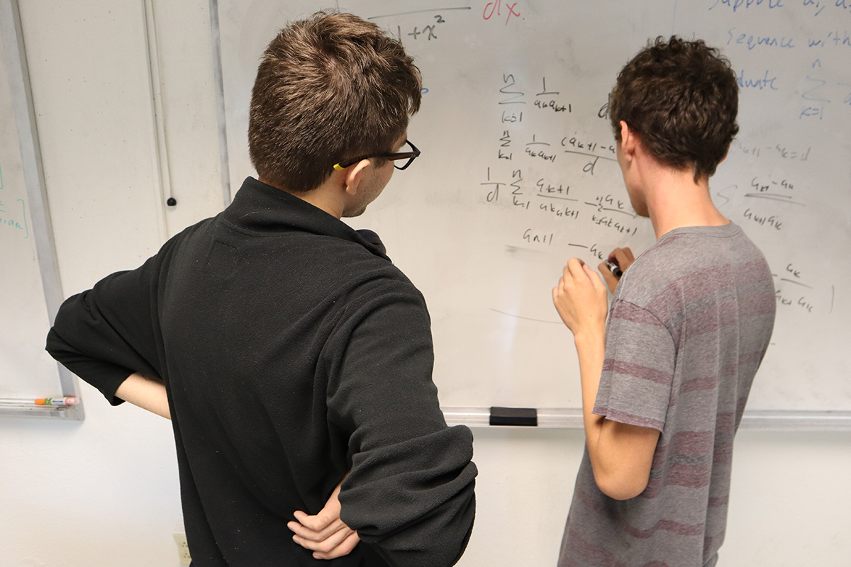 Two students work at a whiteboard on math problems